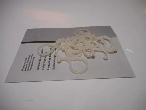 Mehrere transparente Kabelhalter auf einem grauen Untergrund, mit Anweisungen in mehreren Sprachen, die auf eine Verwendung in Verbindung mit Remeha-Geräten hinweisen.